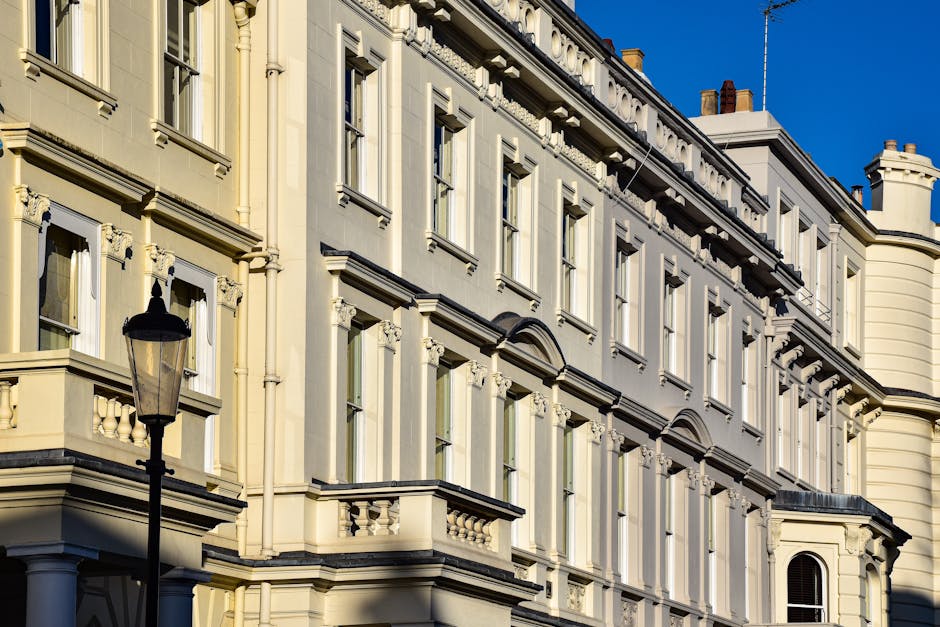 A residential street in Old Brompton Road Earls Court featuring terraced houses with white facades, large sash windows, and decorative mouldings. The pavement on the right side is clean with evenly sp